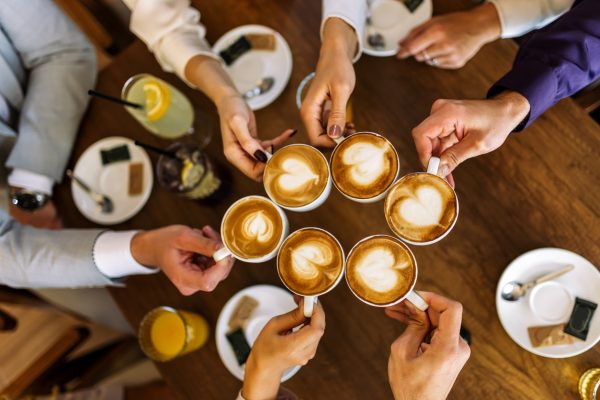 Close-up of friends clinking coffee cups in a cozy cafe.